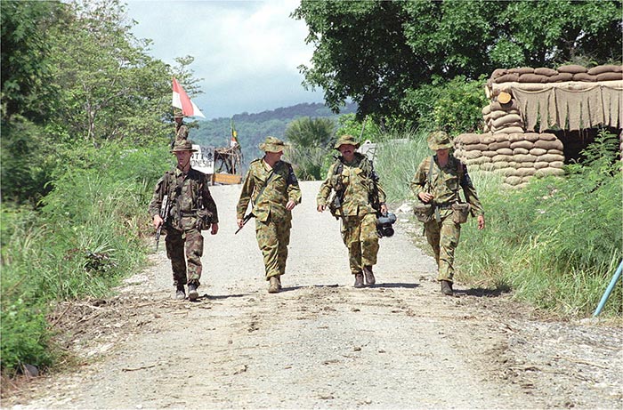 Four armed Australian soldiers walking on the country road