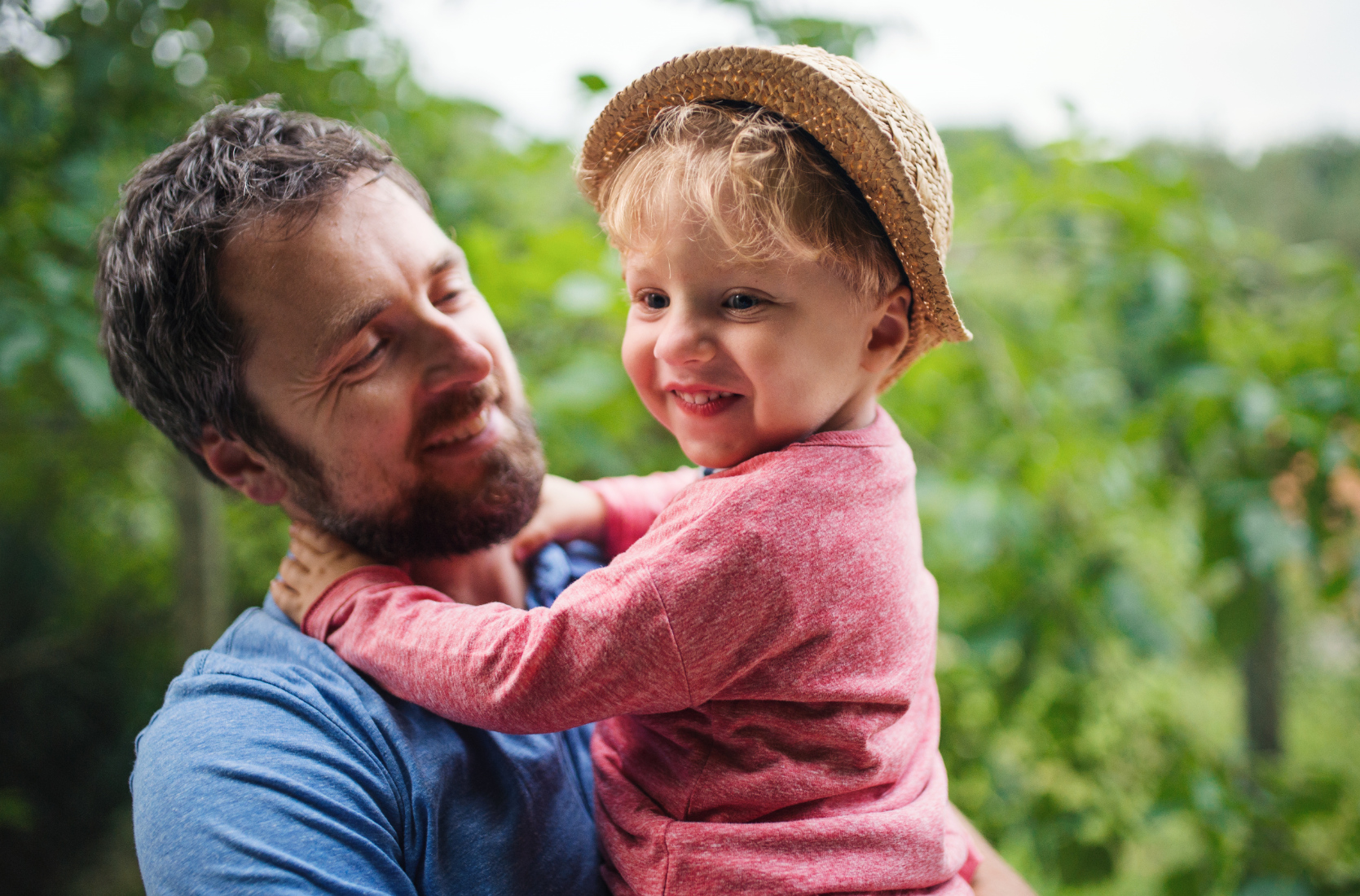 A man holds his young child, both are smiling