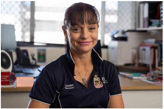 
A photograph of a woman with a dark blue polo and her hair tied back smiling