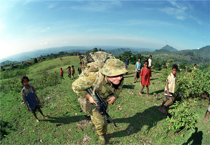 A soldier is walking up a large hill. There are many local children surrounding him