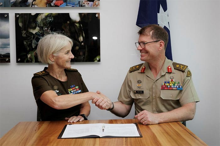 An army female officer shakes hands with the male army officer.