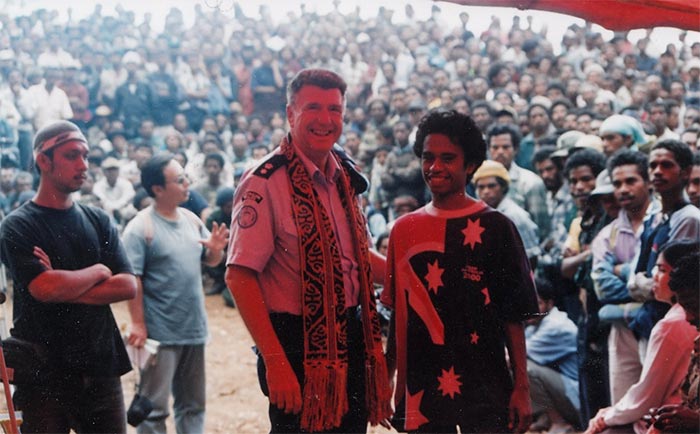 A middle aged man in the police uniform in front of the crowd of East Timorese people.