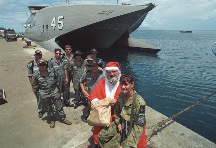 A group of of navy personnel in front of a warship. One dressed as Santa Claus