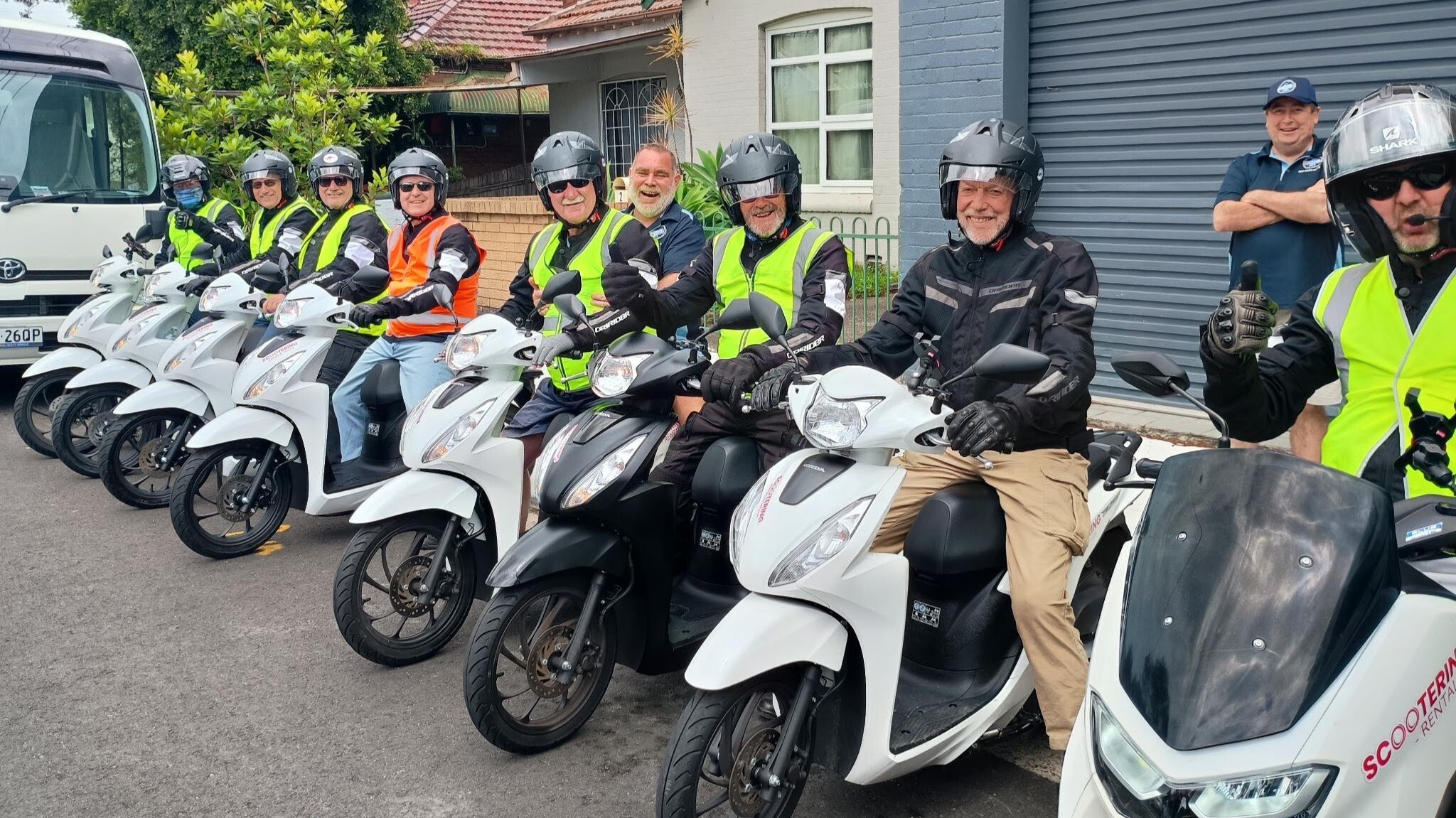 About a dozen men sitting on motor scooters posing for camera