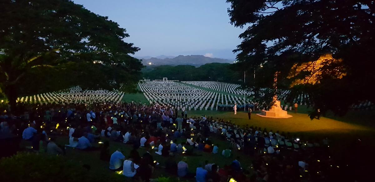 Anzac Day ceremony at dawn with large cemetery in background