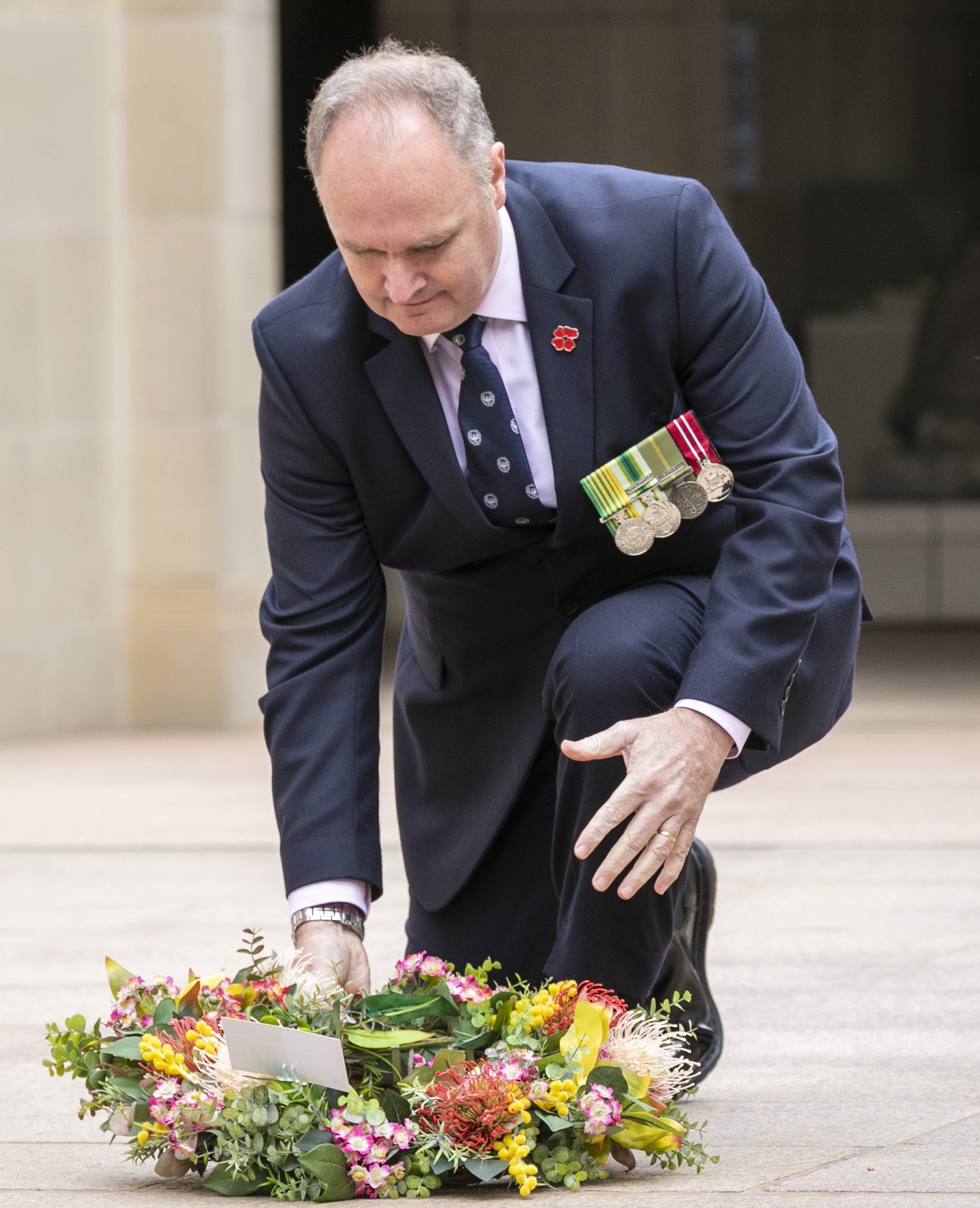 Mr Anderson, dressed in a dark, navy blue suit and tie with four medals pinned to the left side of his chest, laying a wreath on the group.