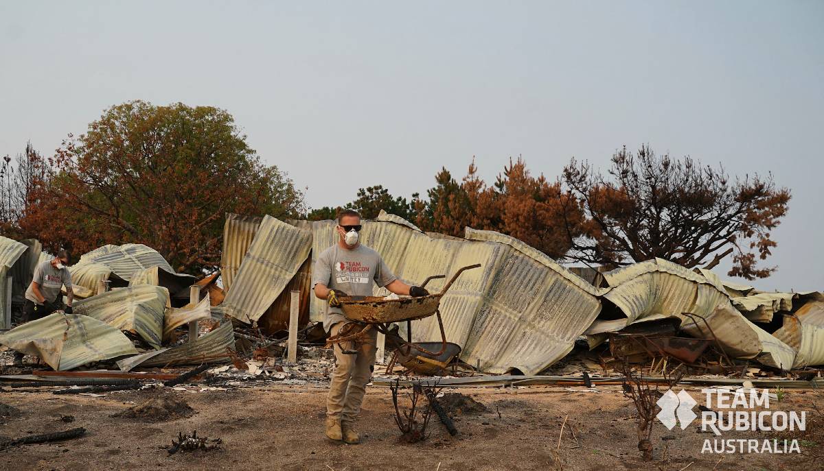 A man in a grey T-shirt and face mask removing material from a burnt-down house.