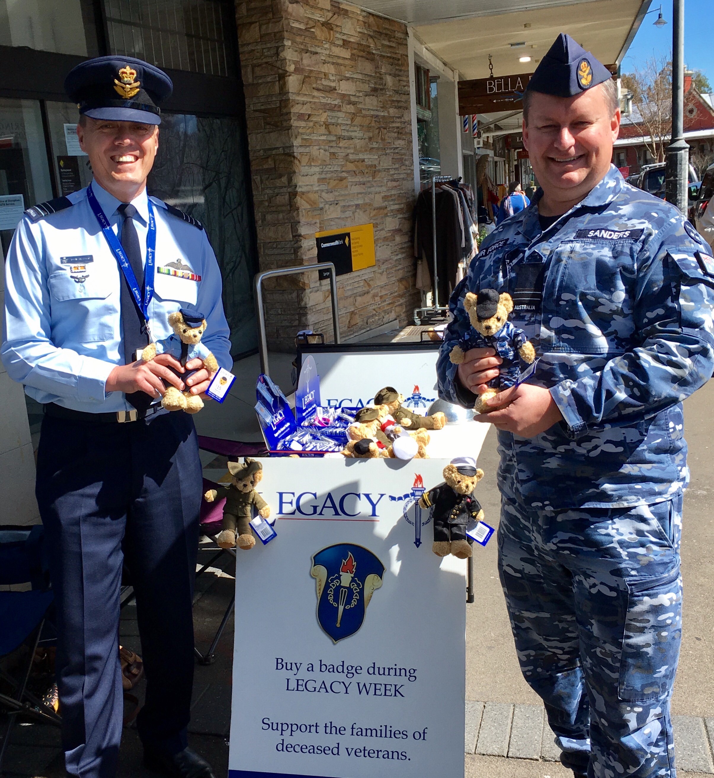 Group Captain Glasson (left) next to a Legacy stand, holding a Legacy bear