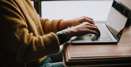 A person is sitting at a desk with a laptop in front of them and their hands are on the keyboard