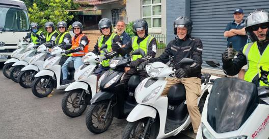 About a dozen men sitting on motor scooters posing for camera