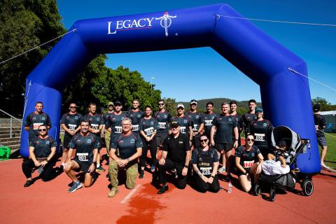 About 20 people posing for camera next to inflatable finish line with Legacy logo on it