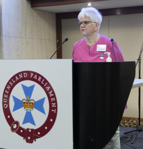 Older woman at lectern with Queensland Parliament sign on it