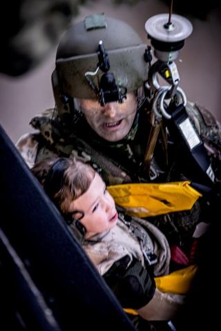 Soldier holding girl, both strapped into winch being raised into helicopter