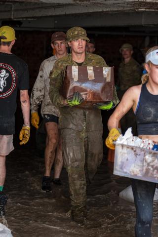 Soldier carrying wet box surrounded by civilians doing similar work