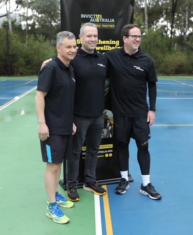 Three men in active wear posing next to Invictus banner