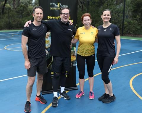 Three men and a woman posing in front of Invictus banner