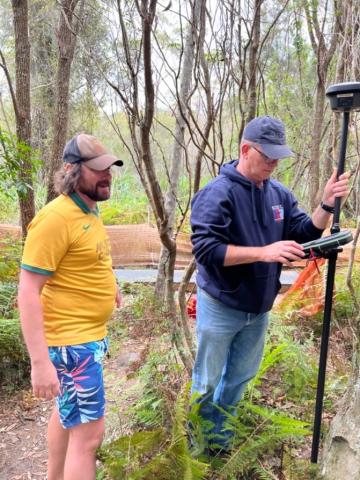 Two men in a forest. One man holds survey equipment.